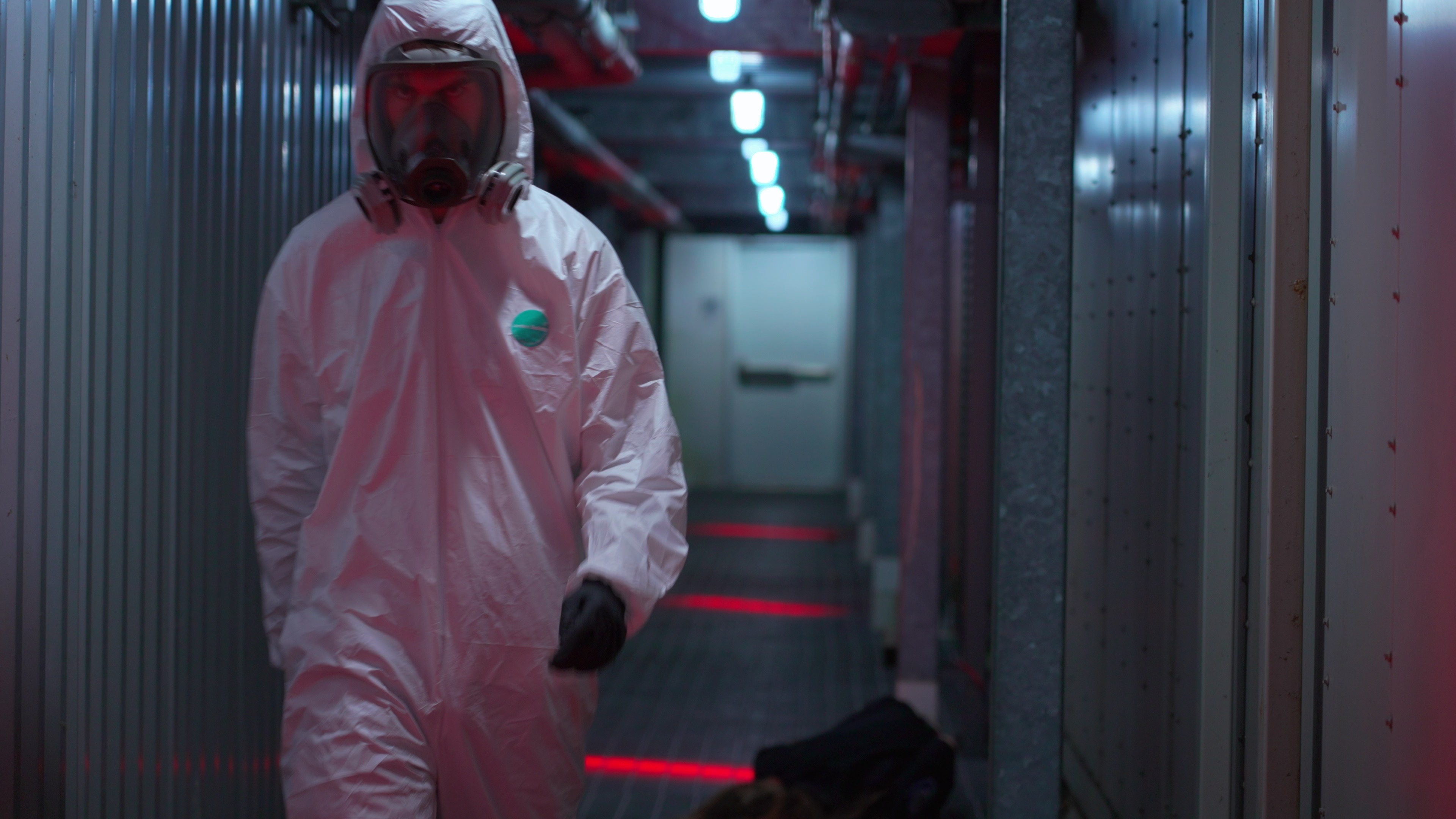 A figure in a biohzard suit walks in the dark